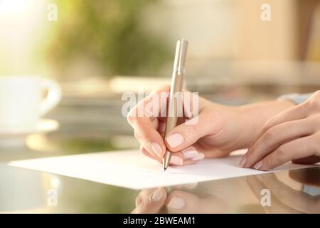 Primo piano di una mano donna che scrive su un foglio su una scrivania a casa Foto Stock