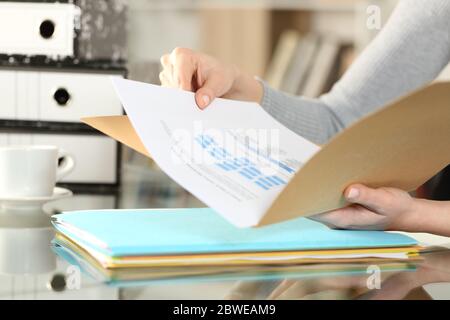 Primo piano di mani di donna che controllano i documenti sulle cartelle seduti su una scrivania a casa Foto Stock