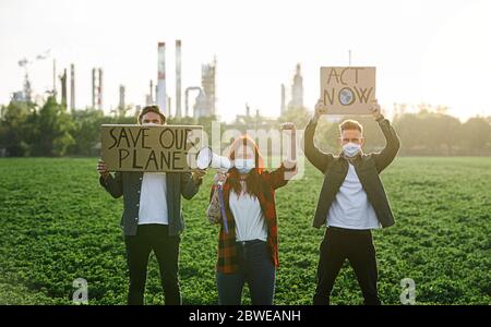 Gruppo di giovani attivisti con cartelli in piedi all'aperto da raffineria di petrolio, protestando. Foto Stock