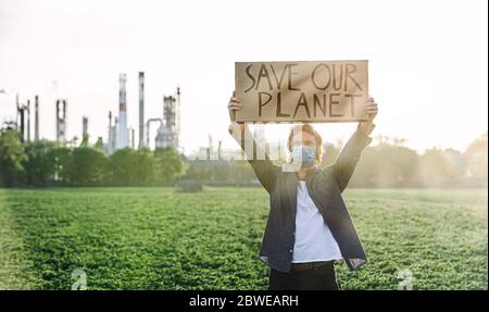 Giovane attivista con placche in piedi all'aperto da raffineria di petrolio, protestando. Foto Stock