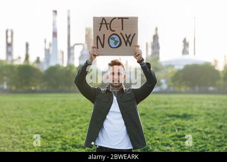 Giovane attivista con placche in piedi all'aperto da raffineria di petrolio, protestando. Foto Stock