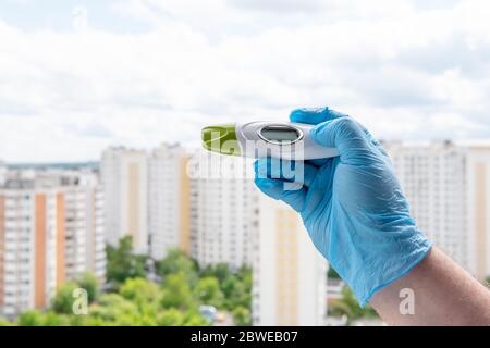 La mano maschile in guanto medico tiene il termometro sul paesaggio urbano Foto Stock