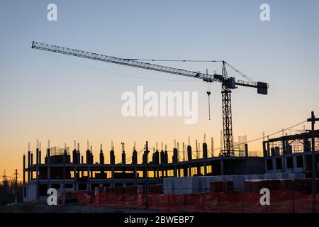 Gru industriali e silhouette di edifici in un cantiere sullo sfondo al tramonto o all'alba. Foto Stock