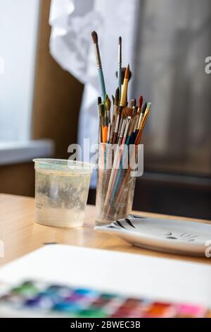 Pennelli per pittura in una tazza di vetro sul desktop. Foto Stock