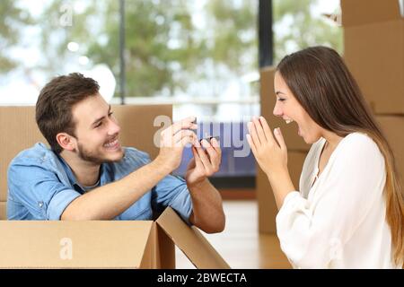 Uomo felice che propone alla ragazza eccitata con anello di nozze mentre si muove in nuova casa circondata da scatole Foto Stock