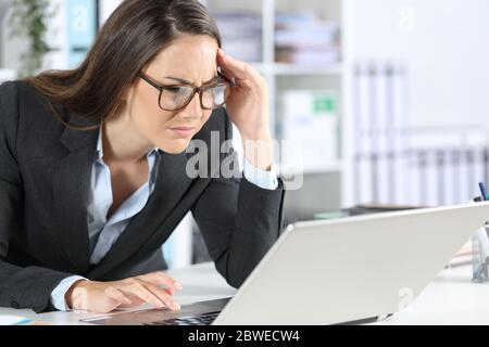Donna executive che indossa occhiali con problemi di vista cercando di leggere sul computer portatile seduto sulla sua scrivania in ufficio Foto Stock