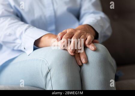 Donna anziana seduta sul divano ha piegato le mani sulle ginocchia closeup Foto Stock