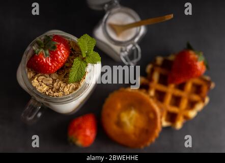 Colazione vegetariana fatta in casa, yogurt con fragole e muesli su uno sfondo scuro tavolo vista dall'alto. Foto Stock