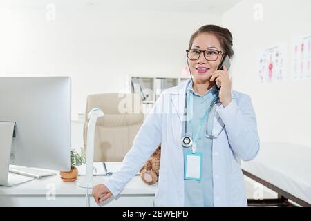 Ritratto di sorridente pediatra maturo che consulta la madre del paziente al telefono Foto Stock