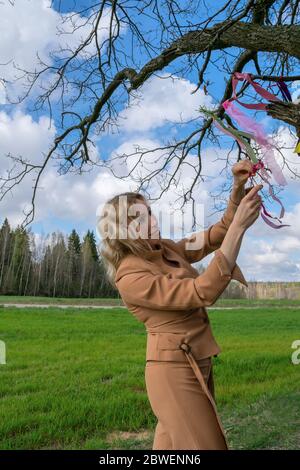 una bionda con capelli lunghi gode di libertà, una donna di mezza età cammina da sola su una strada sterrata tra campi verdi Foto Stock