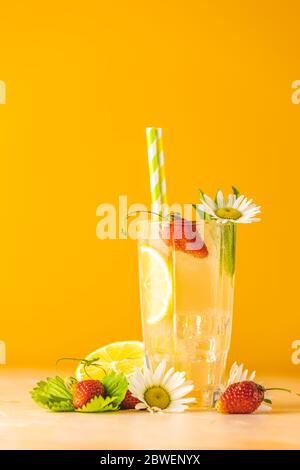 Bicchieri di bevanda rinfrescante ghiacciata con limone e fragola. Sfondo giallo brillante. Cocktail freschi con frutta ghiacciata, erbe e camomilla de Foto Stock