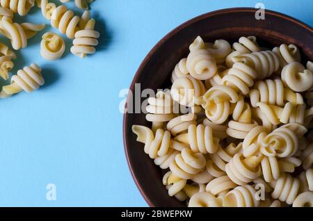 Serve pasta insalatonde non cotta in un recipiente su sfondo azzurro. Ingredienti della cucina mediterranea tradizionale. Gastronomia. Spazio di copia. Clos Foto Stock