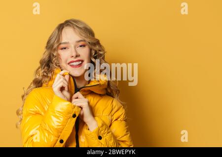 Giovane donna sorridente in giacca invernale su sfondo giallo brillante, primo piano ritratto Foto Stock