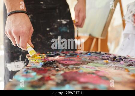 Primo piano immagine di sfondo di artista maschile irriconoscibile mettendo vernice sulla tavolozza mentre dipingendo le immagini in studio d'arte, copia spazio Foto Stock