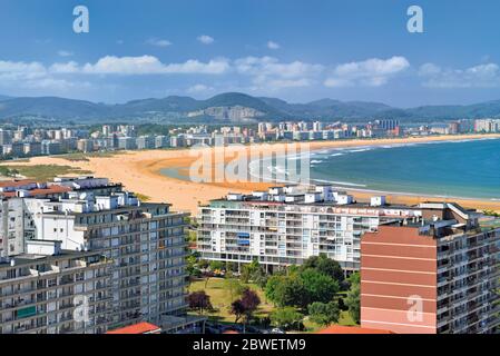 Vista sulla città con ampia spiaggia di sabbia e montagne verdi sullo sfondo Foto Stock