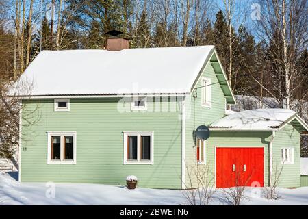 Una casa indipendente, piccola, verde, in legno con porte da garage rosso brillante a Winter , Finlandia Foto Stock