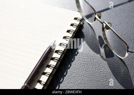 Penna su un notebook a spirale vicino agli occhiali sul tavolo nero Foto Stock