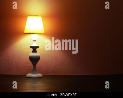 Lampada da tavolo bianca ed elegante con paralume giallo contro parete rossa Foto Stock