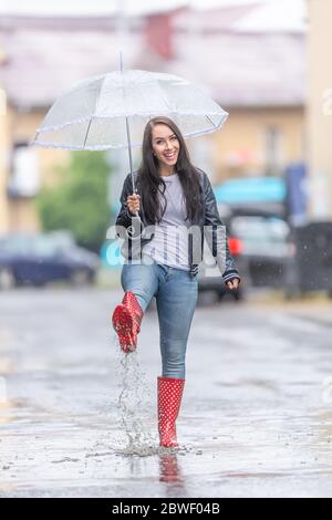 Donna felice in pallini rossi cammina per strada con un ombrello in un giorno raidy. Foto Stock