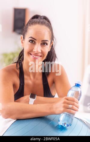 Ritratto di una bella donna appoggiata su una palla svizzera da entrambi i gomiti, tenendo una bottiglia d'acqua. Foto Stock