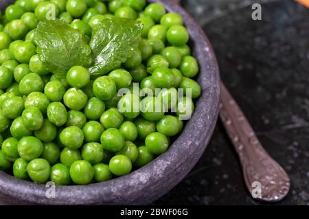 Da sopra ciotola con un mucchio di piselli verdi freschi e foglie di menta messi sul tavolo Foto Stock