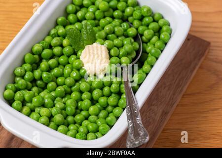 Da sopra contenitore con piselli verdi organici freschi con pezzo di burro e foglie di menta messi sul tavolo copy spazio sullo sfondo a destra Foto Stock