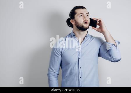 Uomo riuscito con i capelli lunghi sta parlando al telefono ed è sorpreso. Foto Stock