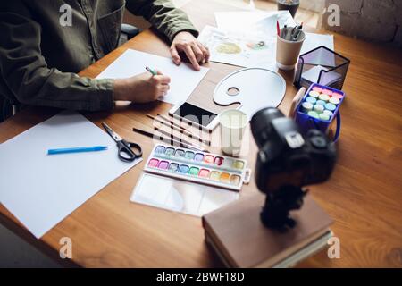 Primo piano uomo che dà lezioni di disegno online a casa. Registrare tutorial per insegnanti su fotocamera per bambini. Digitalizzazione, formazione a distanza. Tecnologie, dispositivi, corsi online dall'atmosfera confortevole. Foto Stock