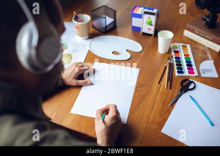 Primo piano uomo che dà lezioni di disegno online a casa. Registrare tutorial per insegnanti su fotocamera per bambini. Digitalizzazione, formazione a distanza. Tecnologie, dispositivi, corsi online dall'atmosfera confortevole. Foto Stock