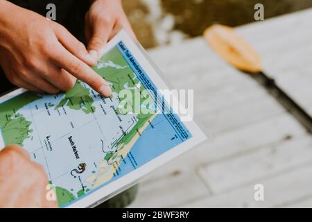Nova Scotia, agosto 2018: Uomo che tiene una mappa, che punta con il dito verso un punto vicino a South Harbor sull'isola di Cape Breton. Concetto di avventura, geocaching Foto Stock