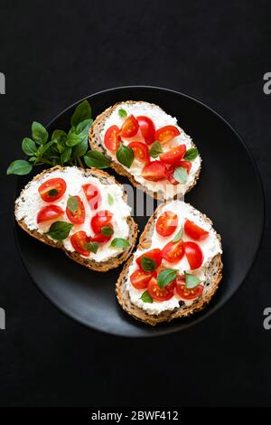 Bruschetta al pomodoro di ricotta con basilico su sfondo nero, Top View Copy Space. Antipasto Italiano Foto Stock