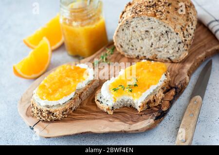 Colazione sana con ricotta e marmellata d'arancia. Pane intero con semi di grano con formaggio bianco fresco e confettura di arance dolci Foto Stock