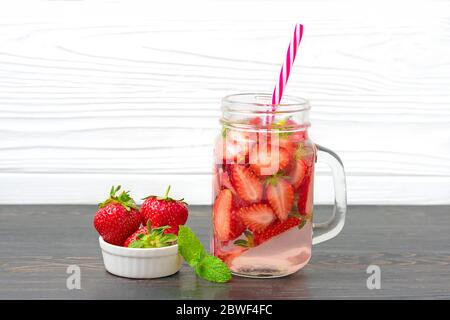 Acqua, cocktail, limonata o tè infusi con fragole. Bevanda fredda estiva ghiacciata con fragola, foglia di menta, cubetto di ghiaccio su sfondo bianco di legno piatto Foto Stock