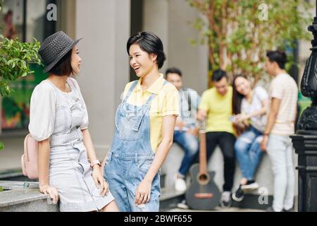 Giovani studenti asiatici che parlano di notizie e gossip quando si è in piedi all'aperto durante la pausa Foto Stock