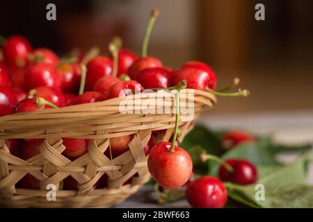 Cestino di ciliegie dolci e mature con foglie su sfondo ligneo Foto Stock