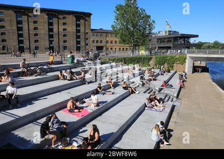 Le persone che godono il sole di Granary Square a Kings Cross, l'ultimo giorno di maggio, come le restrizioni del coronavirus sono attenuate, a nord di Londra, Regno Unito Foto Stock