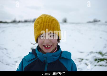 Bambino sorridente felice in cappello giallo all'esterno in inverno freddo nevoso Foto Stock