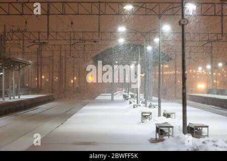 Piattaforma ferroviaria vuota senza passeggeri in bufera/nevicata di notte. Ferrovia, maltempo Foto Stock