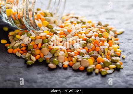 Lenticchie assortite colorate e semi interi di grani versati da un vaso di vetro sul tavolo Foto Stock