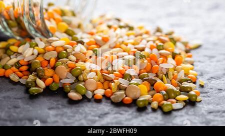 Lenticchie assortite colorate e semi interi di grani versati da un vaso di vetro sul tavolo Foto Stock
