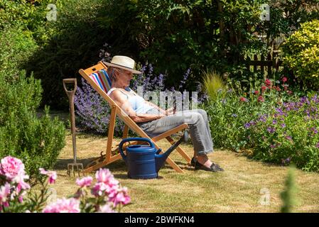 Hampshire, Inghilterra, Regno Unito. 2020. Donna che prende una pausa dal giardinaggio seduto in una sedia a sdraio in una calda giornata estiva. Foto Stock