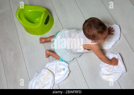 concetto di addestramento del vasino. Un bambino carino in una stanza sul pavimento luminoso gioca con un pannolino e un vaso verde rovesciato. Messa a fuoco morbida, vista dall'alto Foto Stock