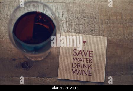 Vista dall'alto di un bicchiere di vino rosso e di un tovagliolo di carta con il testo "Salva acqua, vino da bere" su sfondo di legno. Foto Stock