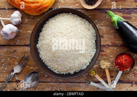 Pilaf ingredienti, riso, verdure, pita, posate, spezie su sfondo rustico Foto Stock