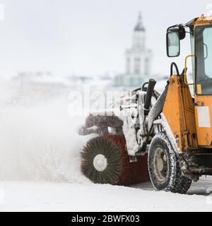 Veicolo per spazzaneve che rimuove la neve dopo la pioggia/tempesta di neve in movimento. Pulizia urgente della strada della città alla luce del giorno. Nevicate pesanti a San Pietroburgo Rus Foto Stock