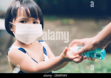 Madre prendersi cura figlio con maschera viso e disinfettante per la protezione malattia influenza o covid-19 all'aperto, mamma e bambino indossare maschera medica mano pulita per s. Foto Stock