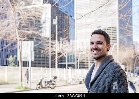 Un giovane sorridente, bearded, in piedi contro gli edifici degli uffici Foto Stock