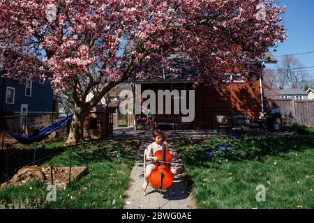 un bambino si siede sotto l'albero fiorito di magnolia nel cortile che gioca violoncello Foto Stock