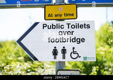 Primo piano isolato UK consiglio segno per i bagni pubblici che dirigono pubblico Signore, signori e utenti disabili su passerella, all'aperto sotto il sole estivo. Foto Stock