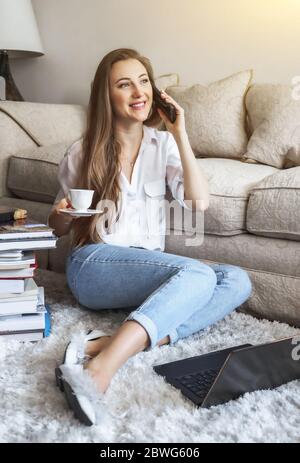 Giovane studente che guarda la lezione online e studia da casa bere caffè. Giovane donna che lavora a casa di frome Foto Stock